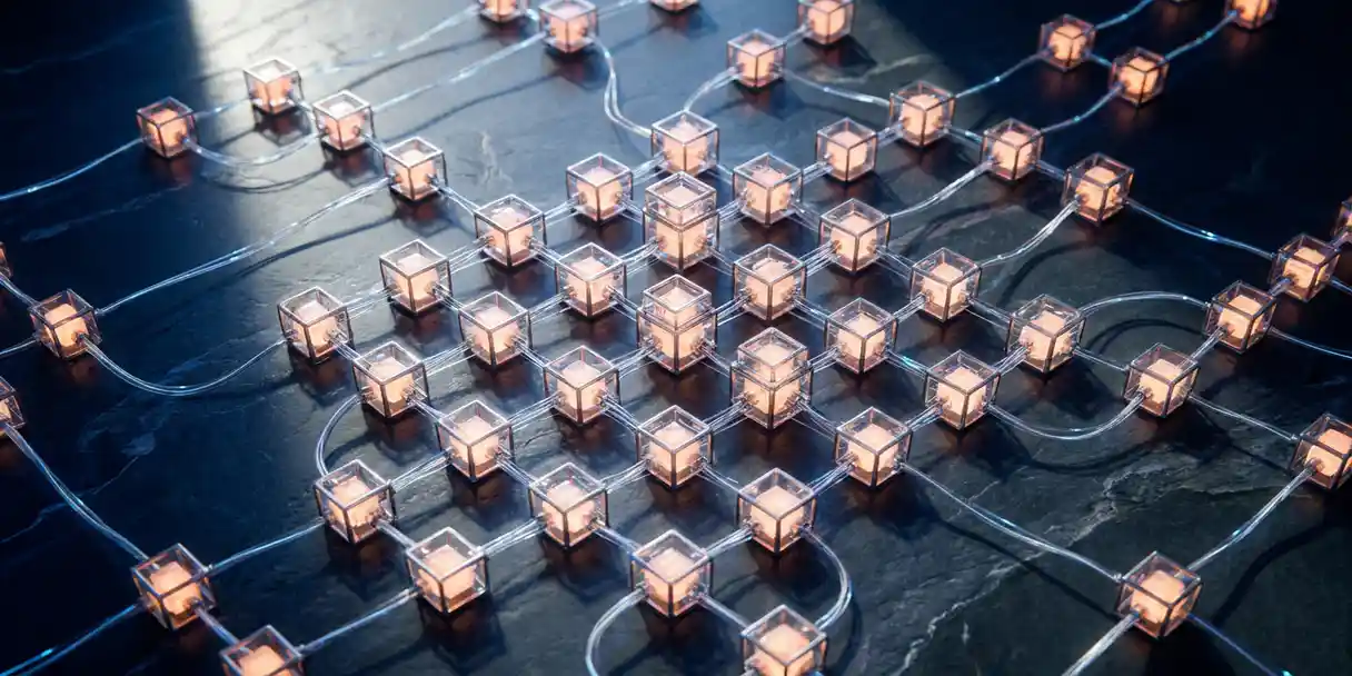 Aerial view of interconnected glass nodes glowing amber, linked by fiber cables across a slate surface in a city-grid data network layout.