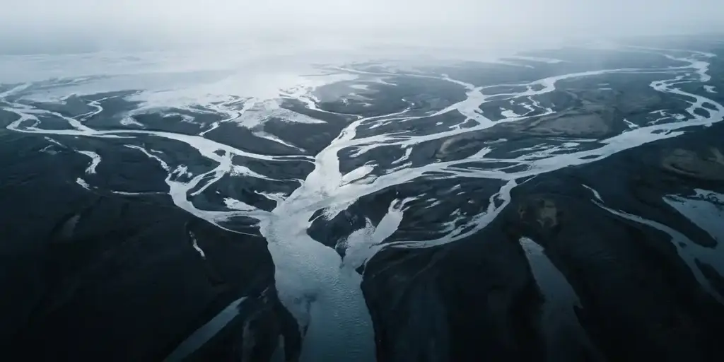 Aerial view of a river delta branching into dozens of streams from a single source, dark soil banks contrasting with silver-blue water channels.