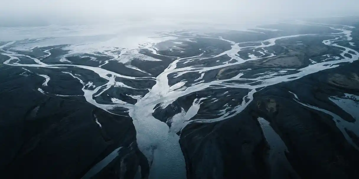 Aerial view of a river delta branching into dozens of streams from a single source, dark soil banks contrasting with silver-blue water channels.
